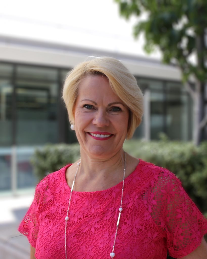 Woman in pink lace top smiling at camera outdoors with modern building background