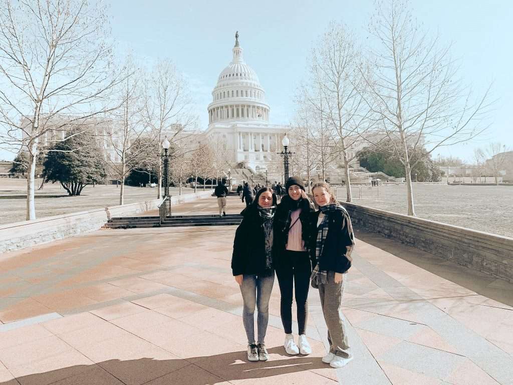 Three women smiling at camera with U.S. Capitol Building in background on National Mall