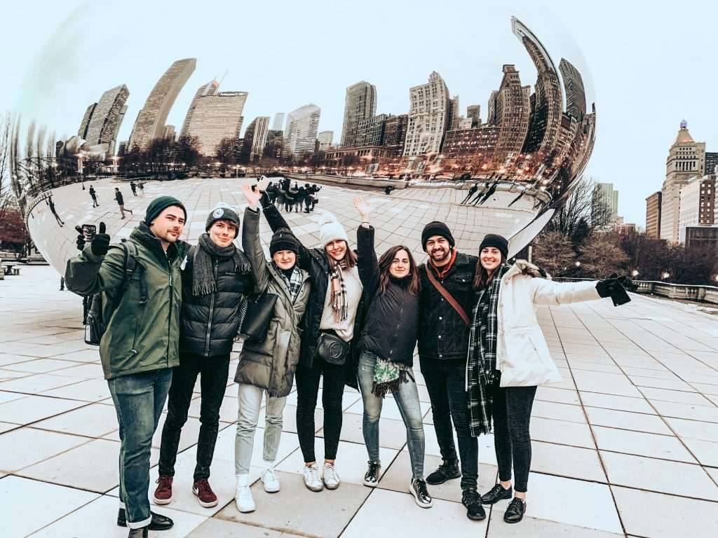 Eight friends posing together at Cloud Gate sculpture in Chicago's Millennium Park with skyline backdrop