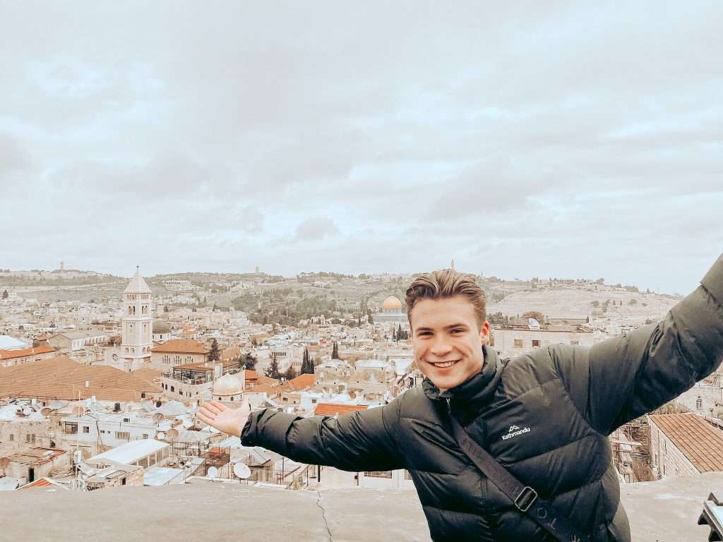 Young man smiling with arms outstretched overlooking Jerusalem's Old City skyline