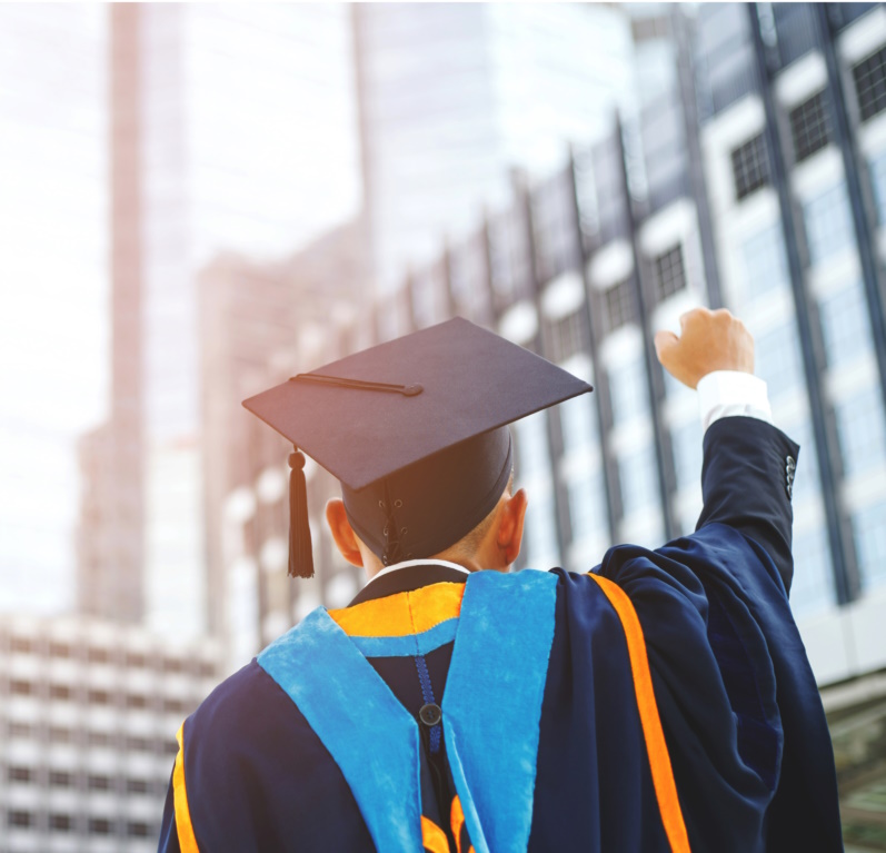 Graduate in cap and gown celebrating with raised fist against city skyline background