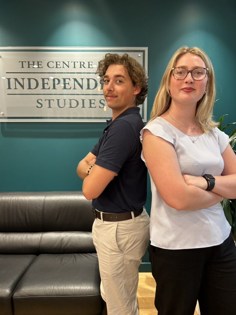 Two people standing back-to-back in front of The Centre for Independent Studies sign on teal wall