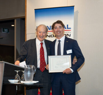 Two men in business suits at an awards ceremony, one holding a framed certificate