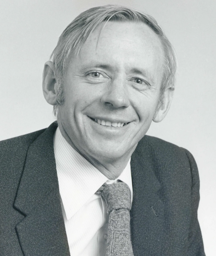 Black and white professional headshot of a man in suit and tie smiling at camera