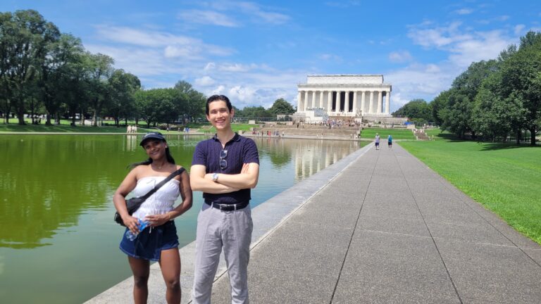 Two people posing on pathway with Lincoln Memorial reflected in pool behind them