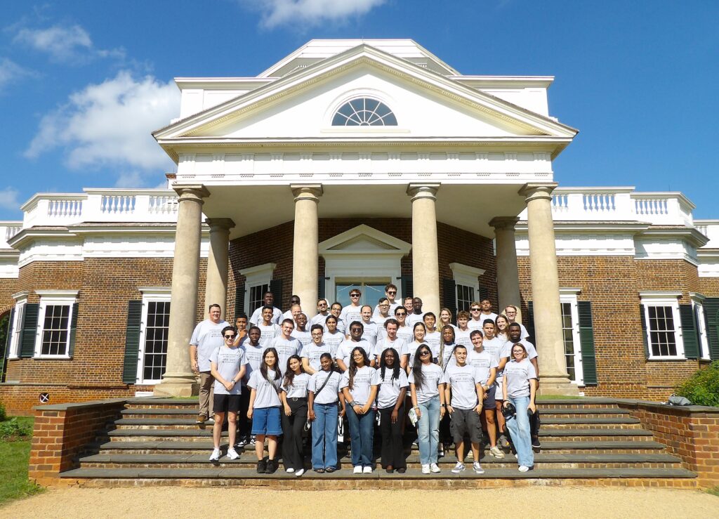 Group of volunteers in white shirts standing on steps of classical brick building with white columns