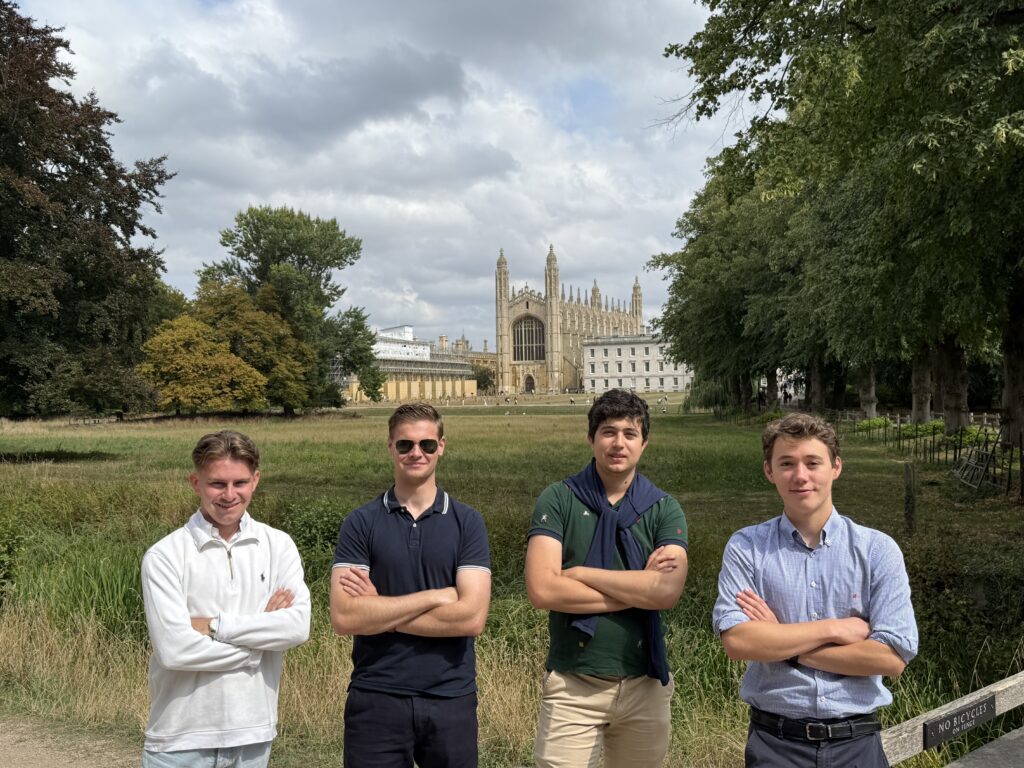 Four young men standing in a field with King's College Chapel Cambridge behind them