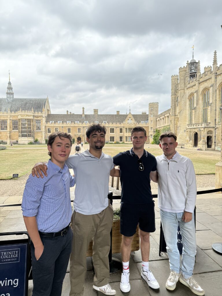 Four young men posing together at Trinity College Cambridge with historic stone buildings behind them
