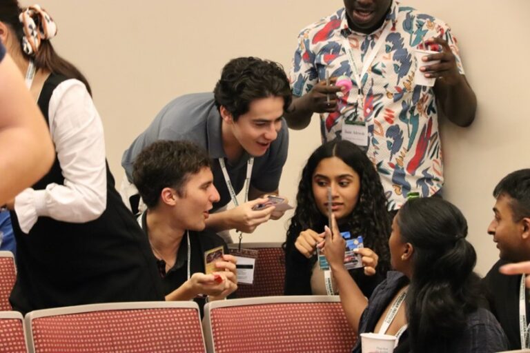 Young adults with ID badges conversing and gesturing animatedly during what appears to be a conference or networking event.