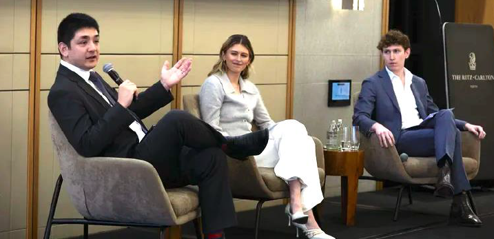 Three young professionals seated in modern chairs during a panel discussion or interview at a conference venue.