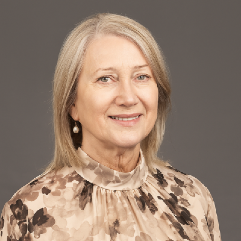 Professional headshot of a woman with blonde hair wearing a patterned top, smiling at camera
